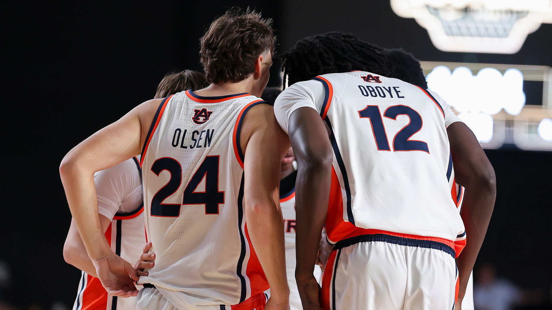 A group of basketball players in white and orange uniforms huddle together on the court during a game.